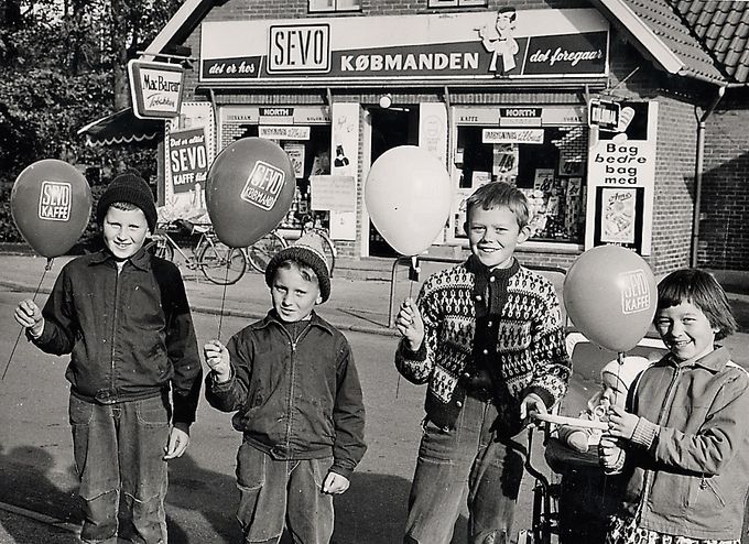 Aase og Svend Aage Madsens købmandsbutik i starten af 1960 ca. Det var dengang, at man stadig havde en rigtig købmandshandel. Hvor købmanden selv fandt det frem, det man havde skrevet op på sin dosmerseddel. Idag skal man i supermarkederne, selv finde tingene og pakke det i en plasticpose.
Vi lever i plasticalderen idag. Der er snart ikke det, man kan få i plastic.