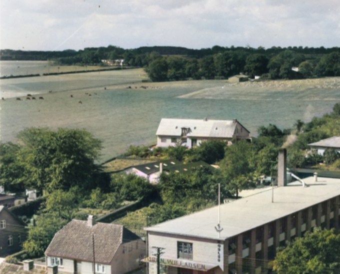  Et helt nyt billede som jeg ikke har set før. Fra cirka 1955.
Søren N. Willadsens Møbelfabrik på hjørnet af Torps Alle og Søndergade. Her med lidt farve.
Øverst oppe i billedet er det Niels Philkærs gård, Taborgård    der ligger. Og hvor hans marker går helt ned til Søndergade. Hvor Malermester  Louis Timmermann, købte et bid af hans mark til at bygge sit hus  i 1957.
På det tidspunkt var der marker og gårde helt til  Skodborg.
 I 7. og 8. klasse på Bakkely skole, var vi ude og prøve et erhverv. Jeg var begge gange på  Philkærs gård, der lå ved siden af Brejdablik og Holger Pedersens gård.
Bag ved fabrikken ligger bungalowen.  Der boede dengang Tapetserermester H. Rolschou Nielsen og
Frisør Fru Rolschou Nielsen 1954. Jeg gik i skole med deres søn   Steen.
Der står.
Willadsens Møbelsnedkeri. Søndergade 40. Søren Willadsen 1880-1956. Derefter Møbelfabrikant John D. Lawaetz 1956-1972. Ti år senere blev han medindehaver af virksomheden som han i 1956 overtog helt. Han drev møbelfabrikken frem til 1972.
Dengang fik træerne lov til at blive store, der var man ikke så træforskrækkede som i dag. Jeg kan ikke lide Stynede træer.
Jørgen Frandsen.
Bare lige en lille tilføjelse. Jeg arbejdede på et snedker værksted i Lindknud efter skolen i perioden 1968-1972. SW var en af de store kunde der, vi var underleverandører af tilbehør, som greb til teaktræskomoder o.l. reol system med tråd ophæng ( meget eftertragtet i dag). Lawaetz leverede også meget andet, som blev lavet i Lindknud. Kryds og bolle spil, tømmerknude, puslespil og bordskånere og meget mere. Alt sammen i de ædle træsorter palisander, mahogni, teak og eg. Alt i massiv træ. De ædle træsorter kom i store læs til SW, som vi så blev hentet til for at læsse af med håndkraft og så skulle de lægges i tørreovn også med håndkraft. Et hårdt arbejde for sådan nogle skoleknejter. Jeg vil nok mene han var datidens TripTrap/Skagerak.
Hanne Ehlers.
Jeg gik i børnehave hos fru Lawaetz på hjørnet af Søndergade/Torpsalle.