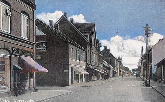 Et billede af Nørregade inden højre side af Nørregade og Jernbanegade blev nedrevet i 1970erne.
Til venstre i billedet er der først Olaf Jacobsens kolonialforretning, så kommer Lindegade og Hans Ehlers installationsforretning. Og ved siden af Ehlers butik var den velbesøgte Biograf Vejen Kino.
Så må det være A/S Centraltrykkeriet og Herre ekvipering handler Paul Høyer, 1954.
Til højre er det fra 1951 avisredaktion på stedet. Tidens tegn, senere var det Aktuelt. Og til slut Folkebladets Redaktion. Og til højre for Bager Sørensen havde Urmager og guldsmed Valdemar Grunnet 1908 - 1973 startet sin butik, fra ca. i 1907.
Som mange billeder på det tidspunkt var der mere ro på end i dag.
Her er der stadig brosten på vejen.
Hanne Ehlers.
Du har helt ret, sikke en ro over det billede.