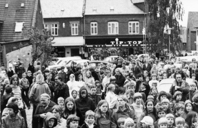 Menneskemængde forsamlet på Rådhus- pladsen i Vejen, 1972. Årsagen til forsamlingen ukendt.
Mon ikke det er børn fra Vejen der kigger ind i 2022 med bekymrede blikke.
Her er et nyt billede af Vejen Kino til højre, og ved siden af H.Ehlers & Søn. Med Lindegade op i billedet.
Sjovt nok ser det ud som om den første Falckstation stadig var der i 1972. 1940 - 1943 Stationsleder Hans P. Nielsen i Lindegade.
Senere i 1950 flyttede Falcks Redningskorps A/S ud til Esbjergvej 2. Falck stationen blev bygget i 1950. Og ved siden af Vejen ny Elektricitetsværk fra 1923.
Vejen Miniby skriver.
Lige fra Værkets Overtagelse (sognets overtagelse af det gamle værk)
havde der været Tale om at bygge Nyt -
- fordi det gamle (hvor Elektriker Ehlers bor) (Nørregade 22) var for lille.
Det viste jeg ikke.
Til venstre for Lindegade er det Tip Top. Hvor
Tage Sørensen åbner butik for herre- og drengetøj i 1960.
Allan Harboe.
Alle har i hvert fald blikket rettet mod det nye rådhus som nu er erstattet af et endnu nyere rådhus.
Blev hele området langs Jernbanegade ikke saneret sidst i 60'erne med plads til rådhus.
På hjørnet af Jernbanegade/Nørregade er der på billedet endnu ikke gjort plads til Aktivbank/Løvbjerg-bygningen som også er/var en flot grå firkantet klods i bybilledet
Kan begivenheden være indvielse af rådhus
- på en kølig sommerdag med blade på birketræerne.