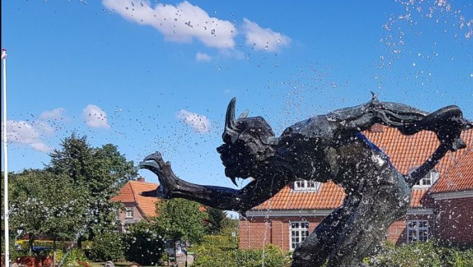 Ole Olesen Sørensen skriver.
Lidt fra forskellige sider på nettet.
Niels Hansen Jacobsen blev født og voksede op på en gård i Vejen. På trods af faderens ønske om, at sønnen blev landmand, valgte han at søge ind på billedhuggerskolen på Kunstakademiet i København, hvor han blev uddannet i årene 1884-1888. Faderen var ikke just begejstret for denne beslutning, og Hansen Jacobsens monograf Niels Th. Mortensen fortæller at: “Selv efter at Niels Hansen Jacobsen havde vundet sig europæisk Ry som Billedhugger, kunde Faderen ikke rigtig tilgive Sønnen, at han havde svigtet Gaarden. Imponeret af Sønnen og hans Værker blev han aldrig - han betragtede ham alle Dage slet og ret som ‘Stenkløver’”. Moderen var derimod en stor støtte, både moralsk og økonomisk, i hans beslutning om at søge ind på Kunstakademiet som 23-årig.
På Kunstakademiet fik han tegneundervisning af Frederik Vermehren og Carl Bloch, mens billedhuggeren Johan C.H. Theobald Stein underviste i anatomi og Vilhelm Bissen i modellering.
På akademiet lærte Hansen Jacobsen bl.a. at beherske tidens naturalisme, hvilket tydeligt ses i hans tidlige værker, eks. skulpturen Loke lænket til klipperne fra 1888-1889, som han debuterede med på Charlottenborg i 1889. Skulpturen er udført i tidens naturalistiske stil og indenfor den herskende traditions normer. Den muskuløse krop er modelleret efter levende model og er stærkt inspireret af Michelangelos to berømte slaveskulpturer (1513-16). Værket vakte stor opsigt, blev købt af Statens Museum for Kunst og indbragte ham både årsmedaljen (Eckersberg Medaillen) og et rejselegat, som førte ham på rejse ned gennem Europa. Med værker som Natten, Skyggen, Friheden og Trold, der lugter kristenblod udviklede han senere sit eget særprægede formsprog, der i mindre grad var præget af tidens kunstneriske normer.
I 1892 bosatte Hansen Jacobsen sig i Paris med sin hustru Anna Gabriele Rohde (1862-1902) - et ophold hvor han blev stærkt påvirket af symbolismen. Hans trang til opgør med den akademiske tradition slog her igennem, og med Døden og Moderen trænger hans forkærlighed for den symbolistiske fremstilling igennem. I denne tid videreudviklede han sin symbolistiske skulpturs formudtryk, som senere skulle blive hans adelsmærke. Fra midten af 1890’erne, under opholdet i Paris, var Hansen Jacobsen ligeledes begyndt at arbejde med keramikken, som blev en livslang beskæftigelse for ham.
Efter hustruens død i 1902 vendte Hansen Jacobsen tilbage til Danmark og levede en delt tilværelse med hjem og værksted om vinteren i København og om sommeren i sin fødeby Vejen. En vigtig bestilling bar ham gennem den svære tid efter hustruens død – monumentet Modersmålet, der i 1903 blev indviet i anlægget ved det historiske samlingssted Skibelund Krat. Samtidig arbejdede han på et monument for Ahlmann til opstilling i Nordjylland samt en mindesten for Cornelius Appel til opstilling i henholdsvis Rødding og Skibelund Krat. I 1908 giftede han sig med Kaja Jørgensen (1882-1928). I årene efter hjemkomsten til Danmark kom et nyt arbejdsfelt til at fylde meget i hans produktion: hugning af grav- og mindesten. De kan ses i mange dele af landet. På Vejen Kunstmuseums hjemmeside er der en kortlægning og beskrivelse af en del af hans grav- og mindesten.
I 1905 var Niels Hansen Jacobsen medstifter af De frie Billedhuggere, som i årene 1905-1913 fungerede som en selvstændig sammenslutning ved siden af Den Frie Udstilling. Et af hans bedst kendte værker var skulpturen, En Trold, der vejrer Kristenkød, som nu står som en del af Troldespringvandet foran Vejen Kunstmuseum og i øvrigt indgik i Vejens kommunevåben.
I 1913 opførte Hansen Jacobsen et atelier i mindelunden Skibelund Krat ved Askov. Dette atelier havde form af en 8-kantet hal og havde også plads til udstilling af hans skulpturer. I 1914 blev atelieret åbnet for publikum. 1923-24 opførtes et museum for Hansen Jacobsen i hans fødeby Vejen. Museet blev indviet 1. juli 1924 og er i dag Vejen Kunstmuseum. En stor del af Hansen Jacobsens arbejder er udstillet dér.
På Vejen kirkegård, hvor Hansen Jacobsen er begravet, kan man se en del af de grav- og mindesten, han huggede til byens borgere.
Bronzeudgaven blev købt af Carl Jacobsen i 1901, efter han havde set den på en separat-udstilling af Niels Hansen Jacobsen. Skulpturen stod på pladsen foran Jesuskirken. Det var dog for meget for nogle; derfor blev den flyttet til Glyptotekshaven. I forbindelse med Ny Carlsbergfondets 100 års jubilæum ville menighedsrådet have skulpturen tilbage til kirkepladsen, men da Glyptoteket ikke ville af med den, blev der lavet en kopi, som blev opstillet foran kirken i 2002.
I 1923 blev der opstillet en kopi foran Kunstmuseet i Vejen som en del af Troldespringvandet. Det er i øvrigt denne kopi, som kaldes Trold, der lugter menneskekød, i Weilbachs Leksikon.
I Vejen er trolden byens vartegn og indtil Kommunalreformen 2007 indgik den i kommunens blå-gyldne byvåben. I 2011 skulle konturen af skulpturen udsmykke en otte-etagers bygning i Vejen ifølge arkitektens udkast. Efter protester fra kristne, der mente at skulpturen var udtryk for kristenforfølgelse, valgte kommunens teknik- og økonomiudvalg at droppe denne udsmykning. Blandt klagerne var formanden for Indre Mission i Vejen, Mona Dahl Nielsen, og Jette Vibeke Madsen fra frikirken Kristus Kirken.
I 1923 blev Hansen Jacobsen bedt om at lave et stykke kunst, der samtidigt kunne fungere som kølebassin til det nyopførte elektricitetsværk i Vejen. Hansen Jacobsen fik lavet en afstøbning af Trold, der vejrer kristenblod der blev placeret midt i et bassin omgivet af fire vandspyende tudser og otte øgler, som Hansen Jacobsen modellerede i beton direkte på stedet. Disse figurer blev med tiden så medtaget af vejret, at de i 2009 erstattet af bronzeafstøbninger efter en bevilling af A.P. Møller fonden.
Det varme vand fra turbinerne i elektricitetsværket blev frem til starten af 1950erne ledt ud i Springvandet året rundt. Om vinteren kunne trolden opleves indhyllet i en tågedis eller pyntet med mægtige istapper.
Efter lukningen af elektricitetsværket har man tilsluttet en pumpe til at holde springvandet kørende. Den kører dog kun i sommerhalvåret.
Troldespringvandet er siden blevet Vejens vartegn og byvåben, indtil kommunalreformen 2007.