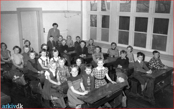 Klassebillede fra Vejen Byskole.
Bemærkning. Fotografiet er indleveret af Helga Ravn, som ses stående i baggrunden.
Jeg er sikker på at der er mange af jer der har gået på Byskolen der nikker genkendende til Lærerinde Helga Ravn.
Det er egenlig utrolig hvor lidt plads man havde dengang til at sidde og skrive ved skolepultene. Mon  ikke   er det på grund af at man skulle fotograferes at man sidder tre.
Man kan købe dem på  Auktioner  i dag.
Der står ved een af dem. 
Gammel skolepult af fyrretræ, med to sæder, skråtstillet skriveplade hvorunder der er rum til blæk og penneholdere. Fra 1900'tallets begyndelse. Der er en hylde under bordpladen til bøger. Bordpladen kan forskydes frem og tilbage.
Her er stadig blækhusene der var noget værre noget at bruge, der var bygget ned i bordene. Særlig pennene havde jeg utrolig svært ved at bruge, enten klattede de med blækklatter eller hvis man skrev lidt hårdt med dem så gik de i stykker. Ja hvis man fik lidt for meget blæk på papiret, havde man trækpapir, der sugede det overskyende blæk op.
Bente Lang.
Pigerne i 1.række er fra venstre Jytte Holgersen, tror det er Anne Lise Frandsen, Jonna Larsen, Else ?, Grete Lauersen, Kirsten Thuesen Lynggård, Conni Michelsen, Karen Margrete Klockmand, Jytte Petersen, Birthe ?, Bente Jensen ( mig) , Rita Gabelgård Nielsen, Gunna Holmgård, Yrsa Ølholm.
Gerda Kristoffersen.
Min lillebror er på billedet, 4. Række , jeg havde også Helga Ravn i 1. Og 2. Og 3. Klasse, den sødeste lærerinde.. Senere efter hun var pensioneret blev jeg besøgsven og hjælper til hun døde i 2003.