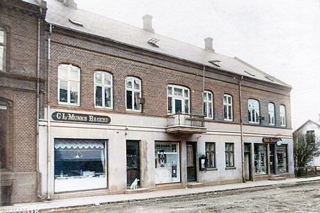 Vejen Arkiv skriver
Nørregade 9, Vejen. Her lå G.L. Munks Bageri, Vejen Broderimagasin og Valdemar Grunnets Urmagerforretning.
Bemærkning. Bagergården blev nedrevet oktober 1979. Sidste ejer Poul Fejfer Jacobsen, Vejen Broderiforretning, Christiane Ahrentz, Urmager Valdemar Grunnet, sidst Margueritten, Åse Petersen. Gavlen der skimtes tilhører Folkebladets redaktionskontor, nu Vejen Centret. I mellem de to bygninger løb bækken, der blev rørlagt i 1909.
.........
Det viste jeg ikke, at der mellem G.L. Munks Bageri   og  Urmager Valdemar Grunnet var en butik med  Vejen Broderiforretning, ved Christiane Ahrentz.
Så der har været tre butikker i bygningen.
Jeg kan heller ikke finde ud af forløbet af Åen 
Jeg viste ikke at der har været et Å forløb der.
Bygningen blev opført i 1878.
Der var stadig jord på vejen dengang.
I 1925  overtog Hans Sørensen Bagerforretningen.
Der var altid en bil med fast chauffør til at få varerne ud med. 
Grotten ved siden af Gartner Falch i Søndergade  ejede Bager Sørensen som en aflægger af Butikken i Nørregade.
Der har jeg købt mange is og rutebiler.
Den lille hund i døren kunne ikke blive kørt over af en bil på det tidspunkt, da der ingen biler var.

