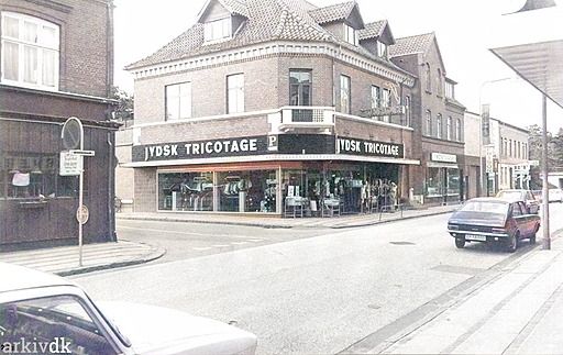  Søndergade og hjørnet op til Jyllandsgade.
Med Jydsk Tricotage som det dominerende i billedet.
John Bent Kristensen skriver.
Hej Johs. Jysk Trikotage på Søndergade 8. er fra 1969.
Ved Inger og Hans Kiilerich, Jysk Tricotage 1969 - 1996.
Annonce i Vejen Avis.
I 1969 greb vi chancen og købte Vejen Sparekasse og efter en gennemgribende ombygning åbnede vi JYDSK TRICOTAGE i ny monterede lokaler med 20 m facader.
RECEPTION
Lørdag d. 28 april kl. 12-14
Indbyder vi forretningsforbindelser, kunder samt interesserede til en uformel reception i vor 