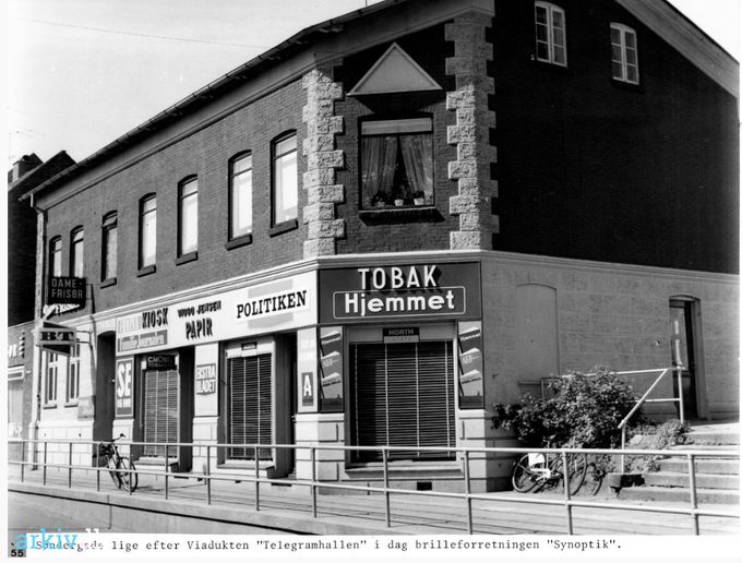 Vejen Arkiv.
,,,,,,,,,
 Et utroligt skarpt billede af  Viggo Jensens Kiosk ved viadukten i Søndergade.  
 Viggo Jensens telegramhal og kiosk. Der var og er fire trin op til Gramhus, og døren som kunderne brugte om søndagen til Viggo Jensen, hvis man ville have Søndags Politiken med den svære krydsord og cerutter til at hygge om søndagen. Han måtte gerne have åbent til baglokalet, og så var der to trin ned til butikken hvor han hentede varerne.  
Viggo Jensens kiosk, som også blev kaldt Basse Jensen. Han havde før han fik kiosken arbejdet på Hansens Hotel hører jeg. 
 Og ved siden af er frisøren Lars P's Hairdesign i dag. Oppe over Viggo Jensens bladhandel var der en damefrisør. Jeg hører fra Linda Jessen der har sin uddannelse som damefrisør der, at navnene var, Ulstrup og sidst i Linda`s læretid overtog Ursula Cordes forretningen. I dag er Linda Kunstmaler.