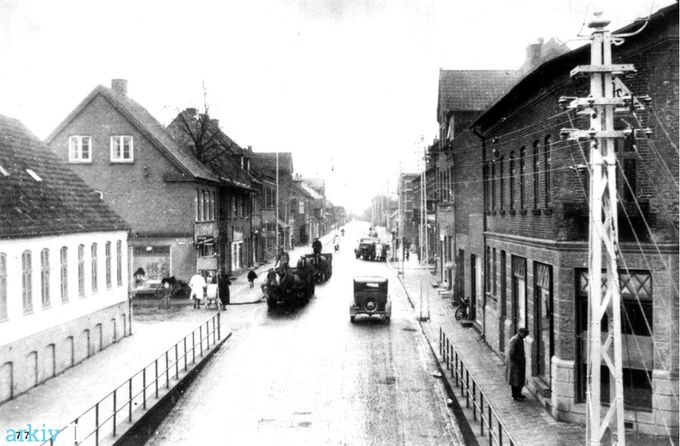Endnu et billede fra Søndergade hvor man endnu kunne se hestevognene og de første HGF høj gammel Ford. Hvor man sagde at  man hurtig kunne fikse bilen hvis den var gået i stå  hvis man havde et elastikbånd og nogle klips.
Henry Ford sprøjtede biler ud på samlebånd. Jeg mener at det var Henry Ford der opfandt samlebåndet.
 Og det siges at de kunne holde evigt i starten. Og det var jo ikke så godt for handlen. Så man lavede det sådan at flere af komponenterne hurtigere blev slidt ned.
Det ser ud til at til venstre for Viggo Jensen, der startede forretningen i 1936 er der et barber skilt. Der har været en frisørbutik i mange år, og er der stadig med Lars P's Hairdesign.
 Søndergade 6 A opført i år 1953.