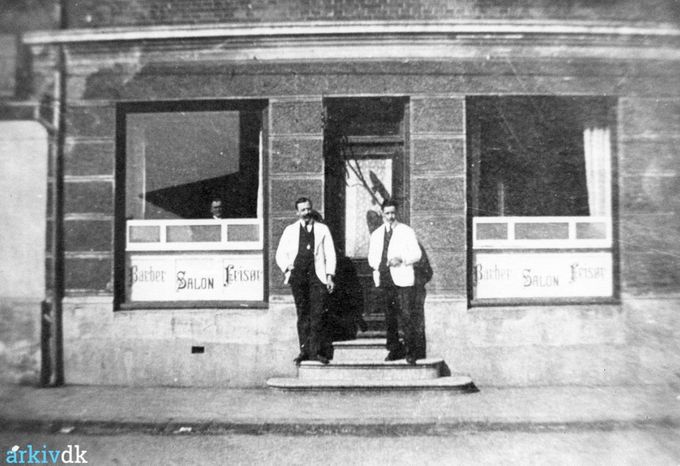 Barber Jørgensens salon. En tid lå salonen Nørregade 3, men den blev blev flyttet flere gange. Salonen blev overtaget af sønnen Hans Henning Jørgensen, som sidst havde salon i Vejen-centret. På trappen står til venstre Barber Christian Jørgensen, til højre H. V. Plambeck.