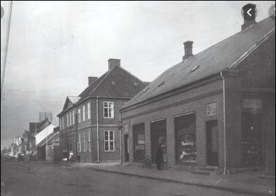 Et dejligt billede af Bruun Møllers boghandel, Nørregade 10, og Mejeriet. Det var Barber Jørgensens far der havde en del af boghandelen. Senere købte Bruun Møller hele huset til udvidelse. Og Barber Jørgensen flyttede over på den anden side af Nørregade. Senere tog begge sønner over i butikkerne, Hans Henning Jørgensen, og Anders Bruun Møller.
