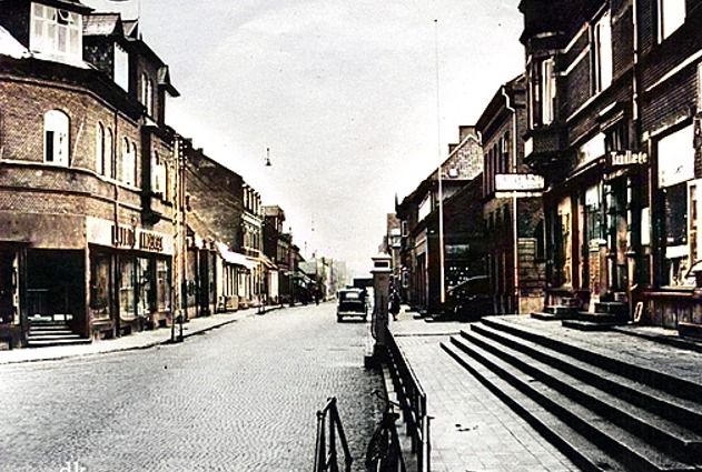 Nørregade i Vejen. Set mod nord fra trappen ved viadukten. 
,,,,,,,,
Til venstre må det være starten på  Laurits Andersens forretning. Det er svært at se hvad der står på forretningen.
I 1924 brolægges Nørregades gade.
Jeg mener at  Manufakturhandler Peter Laurits Andersen startede forretningen i 1938. Han har sikkert snakket med H. C. Hansen der ejede bygningen og hotellet, og huset til højre. Jeg er sikker på at min skolekammerat Per Andersen eller Knud Andersen kan give en god forklaring på at Byens Hjørne, lige er komme til at ligge der. Det er så vidt jeg ved den bedste reklame for en forretning der har været i Vejen.
Nederst ca. midt i billedet er der stadig trapperne op til fortovet. Det var der ikke i 1946 og fremefter. Da der står en cykel kan det jo være at man kunne stille cyklerne der og gå op til forretningerne. Der var Skoletandlæge Nyvad dengang. Det var før Wellness var opfundet med blide toner fra en cd. Det lød nærmest som en boremaskine som man brugte ude på vejen. Og som kunne høres helt ind i venteværelset.
Kim Jakobsen skriver.
Materialisten (Aage Nielsen) og guldsmeden (Arne og Erna Schmidt) var også en del af bygningen med den lange brede trappe. Arne Schmidt  var også ejer af Telefoncentralen der var i gavlen af huset.
Og Jytte Tveen Ørum.
Fru Ingemann var tandlæge ved Nyvad.
I baggården v. Materialisten og Guldsmeden var Jysk Telefon med søstrene Schmidt blandt andet.
Vejen Materialhandel til venstre er fra 1885 og i 1938 overtog Købmand Aage Nielsen forretningen.
Fotograf Kock boede på første Sal, hvor han også havde Atelier. Når man gik op af den meget mørke trappe kunne man hurtig snuse sig til at der boede der en fotograf.
Så kommer Ahornsgade til venstre og Vejen bank med den flotte trappe og flotte jerngelænder, og den store flagstang. Det var min Bedstefar Christian Rasmussen der boede i Allegade der holdt gaden ved banken ren for sne, og sørgede for at flaget kom op på mærkedagene.
Så må det være Bruun Møllers Boghandel der kommer.
