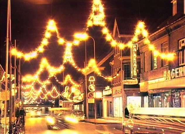 Søndergade i Vejen set mod nord ved juletid H.h. Bageri og Palmehaven 15-13.
,,,,,,
Det er godt nok ikke Jul, men jeg synes dette billede skal med da jeg bliver helt blæst om af de flotte Juleguirlander i Søndergade.
Der står ikke hvilket årstal det er fra, men det var dengang man gjorde meget ud af guirlanderne.
Hvem der havde bageriet den gang til højre ved jeg ikke, måske det var Bagermester Alfred Jørgensen i 1957.
I 1957 var det Restauratør Niels J. J. Varming, der havde Palmehaven. Hvor det virkeligt var startet med Lysreklamer. Også Palmehaven har fået det, og under det står der at der er Bowling.
Så kommer Fredensgade og på den anden side Jensen & Petersen's Herreekvipering.
Og så kommer Elektrikeren, ved Orla Jensen, Søndergade 7 op til 1966. Og derefter Frede Slot 1979.
Der står. Det gik bestemt mod lysere tider, og i 1950’erne, hvor reklamebranchen boomede, kom flere og flere lysreklamer til herhjemme.
Gad vide om de er gået af mode igen, 2022.
Tonny Schwartz.
Når der er bowling tror jeg det er senere end 1957, da det var i en tilbygning, der hvor der senere var diskotek, gætter på en gang i starten eller midt 60erne.
Niels Oluf 'Luffe' Jessen.
Det kunne være en mål at for byen at det komme på den plan igen.
Lone Nørskov.
Disse neon skilte er utrolige smukke lad os få flere af dem.