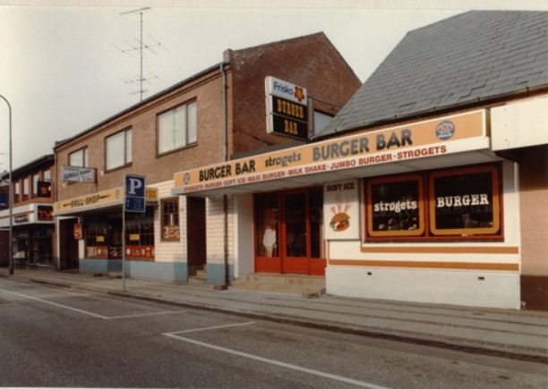 Staub er butikken bag P-skiltet.
Jeg håber at der er nogen af jer der kan udrede billederne.
Lars Ulrik Hoejberg Witter.
Burger baren åbnede Jens Staub i 84’ hvis jeg ikke tager fejl?
Det var på det tidspunkt hvor ‘burgere’ for alvor havde gjort deres indtog i DK og stille og roligt begyndte at ‘tage markedsdele’ fra de mere traditionelle hotdogs og bøfsandwich.
Udover biblioteket var dette stedet hvor en stor del af ungdommen hang ud i start 80’erne.
Flemming Juul Mortensen
Lars Ulrik Hoejberg Witter og i 90'erne.
Lars Ulrik Hoejberg Witter.
Ha!
Jeg kan sagtens huske dig Flemming, fra tiden nede på grill baren. Jeg flyttede fra Vejen i 90’ så jeg er ikke helt skarp på hvad der skete i årene efter.
Arne Beck.
Og i mellem Staub´s burger bar og Frandsen Tv og Radio, lå en slagterbutik. Jeg kan ikke lige huske hvad han hedder. men jeg legede meget med hans pap søn Hans Jørgen Gorm Jensen. Indtil han solgte butikken til Jens Staub.
Tonny Schwartz.
Jeg mener at det var Carsten Ruby der åbnede burgerbaren og senere Giraffen.
Tonny Schwartz.
Jens overtog slagterens forretning og solgte smørrebrød og senere lavede han det om til grillbar, burgerbaren som Carsten startede og som Bjarne overtog, senere havde Hans Marshall og kone den, senere overtog Jens den og lavede en dør imellem ha en smuk dag.
