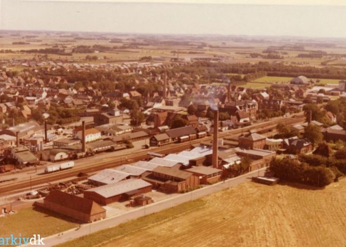 Luftfoto af Margarine fabrikken Alfa og Vejen By.
,,,,,,,,,,,,,
 Her er et nyt billede af Vejen by.
Det er inden at nedbrydningerne af byen gik i gang.
Billedet er fra 1962.
Vejenhallen til højre i billedet blev indviet i 1953. Sjov nok det år jeg som 7 årig startede i Bakkely Skole.
Der var godt gang i skorstenene dengang, jeg kan tælle 8.
Nederst i billedet er det Grønvangs mark, og Margarinefabrikken Alfa med den store skorsten. Helt til højre er det ved den mindre skorsten   fra 1901 med  Johannes Lauridsen`s Cikoriefabrik, med kaffe erstatning. 
Til venstre må de tre skorsten været Phønix Tagpapfabrik.
Midt i billedet er den store skorsten Vejen ny Elektricitetsværk 1923. Der var skyld i at Vejen trolden kom til Vejen. Da der ved den nye Disel motorværksbygning i Lindegade skulle opstilles et Kølebassin i det lille Anlæg med en
Springvandsfigur,  som Billedhugger
Hansen Jakobsen fik til opgave at lave. Så man kunne fint lave både Køle bassinet og trolden som et kunstprojekt.  En meget smart tilgang til at forene det praktiske med det  kunstneriske.  
Den mindre skorsten til højre for El værkes er Andelsmejeriet.  I 1943 overtager Vejen Andelsmejeri huset i Søndergade 39.
Den sidste skorsten midt i billedet øverst  er  FDB’s skorsten.
Dengang var Vejen en lille hyggelig by.