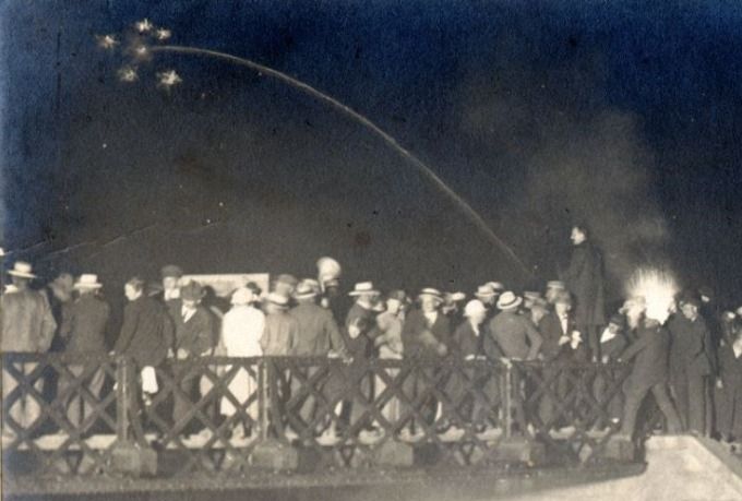 Vejen arkiv skriver.
Skodborghus ved genforeningen 1920.
Bemærkning. Et genforeningsminde fra grænsen ved Skodborghus skrevet af H. Kr. Nissen, Skodborghus Skole. Aftenen før genforeningsdagen den 15. juni 1920, samledes tusinder af nørre- og sønderjyder ved broen over Kongeåen i Skodborghus. På billedet taget fra norden å ses redaktør Ludvig Rasmussen, Vejen stående på broens rækværk, medens han talte til den store folkeskare og samtidig ses en raket suse gennem luften over Kongeåen. Derefter blev der talt af forstander Knud Pedersen, Skibelund Efterskole og både før og efter genforeningsstunden blev der afsunget flere af vore nationale folkesange. Ved 12-tiden stod den store forsamling af grænsebeboere opstillet på Toldvejen med Niels Lauridsens orkester i spidsen og ventede på det øjeblik, da midnatsklokken faldt i slag. På slaget 12 marcherede folkeskaren over broen til musikkens toner af 
