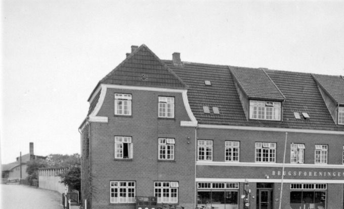Et nyt flot billede af Vejen Brugsforening.
,,,,,,,,,,,,,,,,,,,,,,,,,,,,
Vejen nye Brugsforening er opført i 1913 efter den gamle brugsforenings brand.
Arkitekten var Niels Ebbesen Grue  1879-1937   der også tegnede Brugsforeningen i Askov.
 I 1967 blev  Brugsforeningen nedlagt og i stedet blev der bygget en  administrationsbygning for Phønix  som man opførte man i 1967. 
I dag  huser  Vejen Politi   en køreskole og kontor for Syd trafik den store bygning.
Jeg har altid undret mig over at hvad alt den plads ellers bliver brugt til i bygningen.
Birthe Klockmann Nielsen.
Mange af de ansatte boede der, der var også andre fra byen der havde værelse der.
Erna Ninn Hansen.
Vi boede mange i Vejen Brugsforening, især før der kom selvbetjening. På første sal boede min familie (far, mor + 5 børn) - desuden brugsens bogholder+ kasser.
På øverste etage boede største delen af personalet + to tjenestepiger.
Personalet fik vasket sengelinned + kitler, og der blev serveret mad 6 gange om dagen (morgen, formiddag, frokost, eftermiddagskaffe, aftensmad + aftenkaffe). Det var et travlt hus, men jeg husker det som en hyggelig hverdag, hvor alle var som en stor familie.
