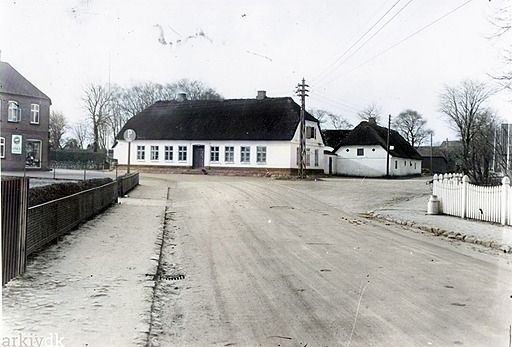 Gården Birkely, på hjørnet af Nørregade/Baungårdsvej før nedrivningen i midten af 1930'erne. Set fra Frd.VII's gade
Fotograf K. H. Kock Vejen.
,,,,,,,,,,,,,,,
Der står i Folkebladet  som jeg savner meget.
Der kan det med underfundig humor.
Ved Gennemførelsen af Amtsvejen gennem Læborg til Asbo har højere Magter inden for
Vejvæsenet bestemt, at Gaarden ”Birkely” af Hensyn til Oversigten skal nedrives, og som
bekendt har Vejen Sogneraad af Vognmand J. H. Klockmann købt Arealet. Udbygningerne er man i Gang med at nedrive, og længe varer det ikke, før ogsaa det smukke Stuehus
forsvinder.
I den sidste Tid er der ofte over for os fremsat Ønske om, at der blev gjort Forsøg paa at
redde denne gamle, særprægede Bondegaard; men der er intet at gøre. Amtsvejvæsenet har
stillet bestemt Krav om Nedrivning under Henvisning til, at Overvejinspektøren som Betingelse
for Tilskud til det store Vejarbejde havde fordret, at der paa dette Sted blev fri Bane. Man kan
mene om Forholdene, hvad man vil; men en Kendsgerning er det, at de Ændringer og
Forbedringer, der i de senere Aar er gennemført, har tilvejebragt Forhold, saa det stærke og
ubetingede Krav om Nedrivning ikke er særlig godt underbygget. Maaske Faren endog
forstærkes, naar Banen bliver ”fri” og en stærkere Gennemkørsel Følgen.
 Den smukkeste Bygning i Vejen forsvinder, og Jorderne sammenlægges med Arealer ved
Baungaardsvej, der tidligere har været underlagt den Ejendom, som Hestehandler Munk ejede.
,,,,,,,,,,,,,,,,
Til venstre var på den tid i 1938 Købmand Jens P. Simonsen. Og  i venstre hjørne må det være indgangen til Den gamle byskole.
Til højre står der en mælkejunge, som jeg kan huske fra min barndom, på Askovvej hvor gårdene skyllede mælkejungerne rene til næste påfyldning af mælk  og som kunne høres i hele gaden. med en speciel lyd som jeg ikke har hørt siden.
I dag er de samleobjekter fra en tid der var.
Her på billedet kan man rigtig se gaden og fortovet inden der kom brosten på, det skete i 1924.