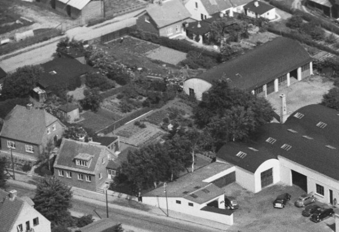 Sådan så det ud da jeg startede i Bakkely Skole i 1953.
Ja der var ikke lyskryds ved enden af Askovvej og ud til Søndergade.
De to huse til venstre op af Askovvej er der, og på hjørnet af Askovvej og Allegade er det Kristian P. Petersen`  hus og værksted, med en sort træbygning i nummer 23     i Allegade, hvor jeg i min barndom var inde for at købe lister til mine mange drager der blev sat op på Grønvangs marker. De blev savet ud af en drabelig rundsav, som jeg stod på tilbørlig afstand fra.
 Karetmager P. Petersen var fodboldspiller på førsteholdet i sin ungdom i Vejen.
Da jeg startede mine gåture ned til mine bedsteforældre i Allegade 17, kom jeg forbi hans hus der lå på hjørnet af Allegade og Askovvej. Der var et mærkeligt køretøj der i mange år var en kilde til forundring hos mig.
Siden fik jeg at vide at det var en Gig.
Gig,   tohjulet personvogn  til en hest som trækker den.
Da jeg startede mine ture derned i slutfyrrene var møllen og skorstenen væk. Så det er først i dag at jeg ser hvad der har været.
Huset oppe til venstre er mine bedsteforældres hus nr. 17.  Magrethe og Christian Rasmussen. 
Tilbage ved Ford ligger Læge I. C. Heuch  Bolig der havde en meget flot have, der senere blev til en parkeringsplads.
  Her kan jeg i 2020 for første gang nogensinde se Ole Haagensens villa i Søndergade fra havesiden fra 1949. nede til højre hjørne.
Det har været et   meget flot hus i sine velmagtsdage, og sikke en flot have idyl. Der var mange træer dengang, som en naturlig del af bybilledet. Haven er meget større end jeg har forestillet mig den.
Frank Nielsen. Deres svigersøn Frode Pedersen tager noget af et indhug af deres have, da han bygger hus og garage til hans vognmands forretning en gang i 60` erne.
Fru  Inger Marie Haagensen boede alene i huset i mange år, og kom godt op i årene.
Nede i venstre hjørne er det   Conrad P. Møller & Søn. Autohandel.
Det tredje hus ned af Søndergade er  det gartner Falk. Jeg var inde hos ham for at købe persille, så siger han jeg har desværre ikke mere, og dog vent lige et øjeblik. Så gik han ud i sin have og plukkede frisk persille til mig.
Og ved siden af ligger lidt tilbage Grotten, der var en aflægger af Bagermester Hans Sørensen i Nørregade.
Den lange sorte bygning  oppe til højre i billedet var Trælasten der fyldte hele den ene side af Allegade, ned til Jyllandsgade.
Ulla Hübertz Madsen skriver.
I nr. 2 fra Ford er jeg født . Stien mellem gartner Falck og huset føre op til min fars værksted, hvor han sprøjtemalede biler for Ford.
