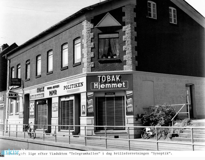 Telegramhallen ved viadukten i Søndergade.
,,,,,,,,,,,,,
Et nyt klart billede af
Telegramhallen ved viadukten i Søndergade.
Der står.
Søndergade 4 efter en ombygning i 1949.
Og man kan købe Familie Journalen, Politiken, Nationaltidende,
Hjemmet og Ude og Hjemme.
Viggo Johannes Jensen, kaldet Basse, der var hotelkarl på Hansens Hotel, købte i 1936 Telegramhallen i Søndergade 4. Hans kone Abeline Cecillie Håhr Høj, født i Lønne var servitrice på Hansens Hotel.
Deres tvillinger Elly og Grethe var født i 1934. For at forretningen kunne drives var det nødvendig med en ekstra indtægt, så Viggo Jensen måtte tage arbejde på Alfa, samt passe regnskaber på Hansens Hotel.
Det var i Telegramhallen man solgte biletter til de 4 store teateraftner på hotellet. Det var meget
aktraktivt i det folk tog plads i liggestole for at få de bedste pladser.
Der var mange lejligheder i huset, Harry Weis havde i en årerække klinik, ligesom frisør Cordes havde salon.
Op af trapperne til højre var der en bagdør man kunne gå ind af og købe aviser om Søndagen.
Ca. i 1977 blev kiosken nedlagt.
Birgit Kahr.
Et fantastisk godt billede. Og der er så mange minder derfra. Vi kunne jo også næsten se derned fra vores stuevindue øverst på Rolighedsvej.
John Bent Kristensen.
Vi boede der fra 1974-1977 i lejligheden ved BT skiltet, der var støj fra Hovedgaden, jernbanen, og fra værtshusene, men vi mærkede det aldrig, en rigtig god tid.